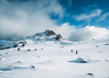 Two people walking up a mountain with snow gear