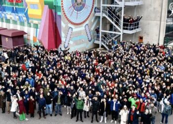 Part of the members of the ATLAS collaboration in front of the ATLAS experiment mural (1:3 scale) and ATLAS control room located at CERN, 100 meters above the experiment cavern.