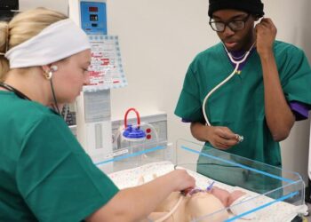 Students practice listening to the heartbeat on a model baby.