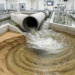 Pipe placement at a sharp bend exit reshapes downstream scour under unsteady flows